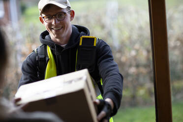 Freundlicher männlicher Kurier, der ein Paket an der Haustür abliefert - CAIF32074