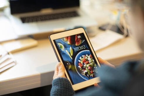 Woman looking at takeout menu on digital tablet - CAIF32078