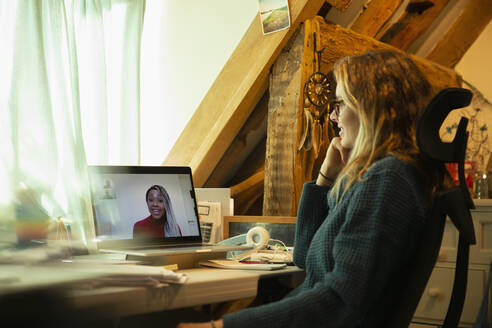 Woman video chatting with colleague on laptop screen in home office - CAIF32095