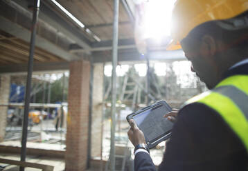 Male architect looking at digital blueprints at construction site - CAIF32138