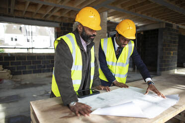 Male architect and foreman looking at blueprints at construction site - CAIF32147