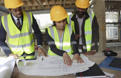 Architects discussing blueprints at construction site - CAIF32161