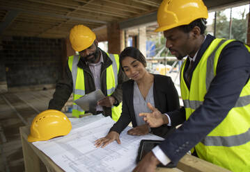 Architects and engineer discussing blueprints at construction site - CAIF32166