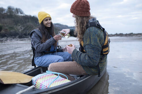 Happy young couple drinking wine in canoe on beach - CAIF32216
