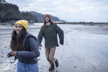 Happy young couple running on wet sand beach - CAIF32223