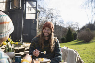 Glücklicher junger Mann beim Frühstück vor einer winzigen gemieteten Hütte - CAIF32228
