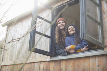 Portrait happy young couple in tiny cabin rental window - CAIF32233