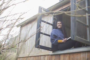 Happy young woman in tiny cabin rental window - CAIF32234