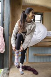 Junge Frau beim Anziehen von Socken in einer winzigen Miethütte - CAIF32245