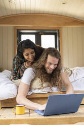 Glückliches junges Paar benutzt Laptop in kleiner Hütte - CAIF32251