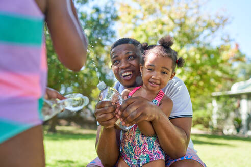 Glücklicher Vater und Töchter spielen mit Spritzwasserflaschen - CAIF32271