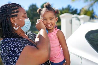 Portrait mother helping cute toddler daughter with face mask - CAIF32288