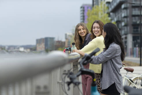 Glückliche junge Frauen, die sich an einem städtischen Geländer anfreunden - CAIF32325