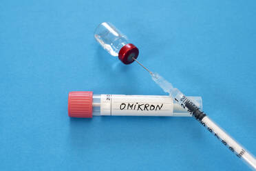Medizinische Spritze in Fläschchen mit Omicron-Tupferröhrchen vor blauem Hintergrund - DRF01786