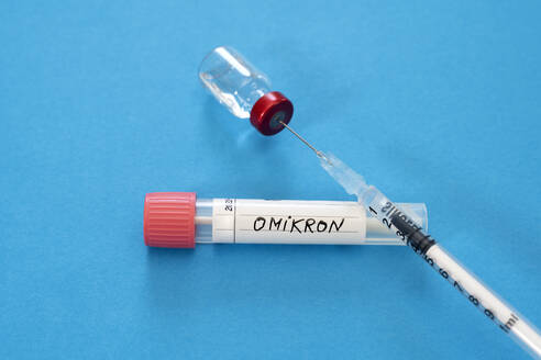 Medical syringe in vial with Omicron swab tube against blue background - DRF01786
