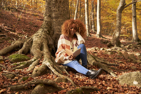 Junge Frau liest ein Buch in einem Baum im Herbstwald - VEGF05250