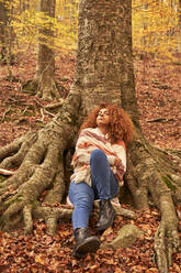 Junge Frau entspannt sich an einem Baum im Herbstwald - VEGF05252