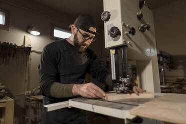 Woodworker working on band saw in workshop - LLUF00434