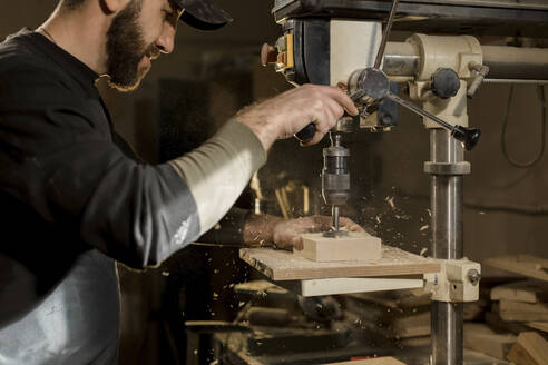 Handwerker bohrt Holz mit einer Maschine in der Werkstatt - LLUF00435