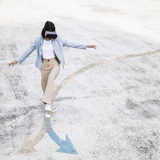 Teenage girl wearing virtual reality simulator walking on arrow symbol - UUF25292