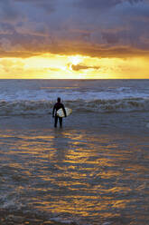 Man with surfboard looking at dramatic sky over sea - OMIF00258