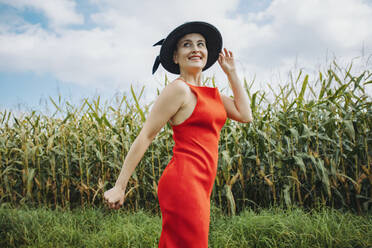 Lächelnde schöne Frau mit Hut vor einem Maisfeld stehend - AANF00253