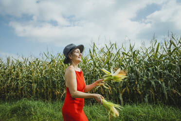 Frau mit Hut und rotem Kleid jongliert mit Hühneraugen auf einem Feld - AANF00255