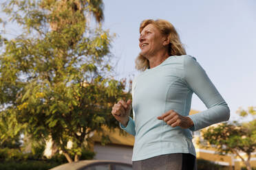 Lächelnde aktive ältere Frau beim Laufen im Park - TYF00060