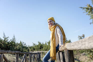 Smiling woman with scarf leaning on wooden bridge - EIF02805