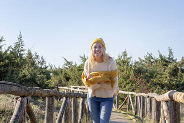 Smiling woman with scarf standing on wooden bridge - EIF02808