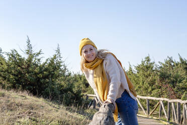 Woman in knit hat and scarf leaning on wooden bridge - EIF02809