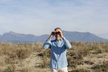 Mann schaut durch ein Fernglas in der Wüste stehend - EIF02810