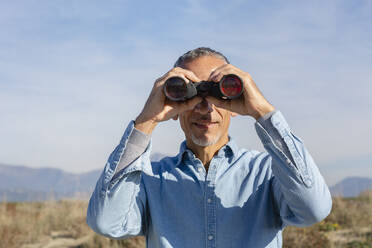 Man looking through binoculars on sunny day - EIF02812
