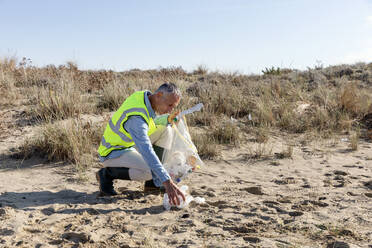 Mann sammelt Müll kniend auf Sanddünen - EIF02830