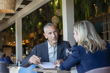 Businessman explaining contract to client sitting in restaurant - EIF02840