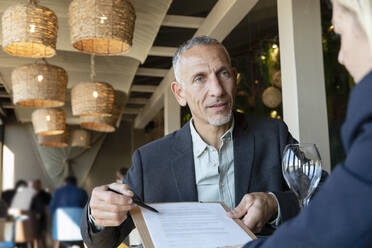 Businessman showing contract to client in restaurant - EIF02842