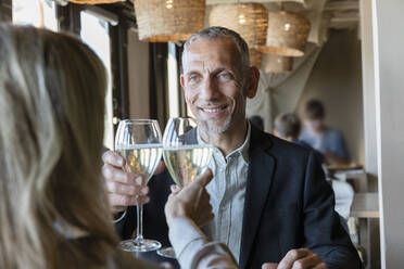 Lächelnder Mann stößt mit einer Frau beim Mittagessen im Restaurant mit einem Glas Champagner an - EIF02847