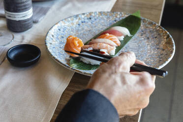 Mann hält Sushi auf Stäbchen im Restaurant - EIF02850