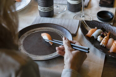 Frau hält Sushi mit Stäbchen im Restaurant - EIF02853