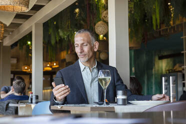 Geschäftsmann schaut auf sein Smartphone im Restaurant - EIF02856