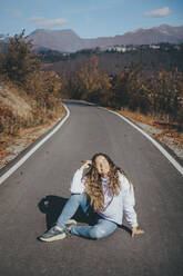 Thoughtful woman sitting on road - OMIF00263