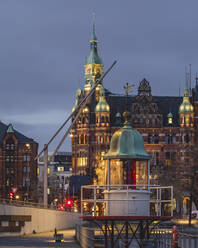 Germany, Hamburg, Speicherstadt district at dusk with lighthouse in foreground and town hall in background - KEBF02114