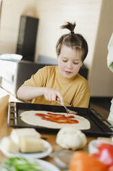 Junge bestreicht Pizzateig zu Hause mit Soße - SEAF00258