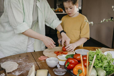 Frau unterrichtet Jungen beim Schneiden von Tomaten zu Hause - SEAF00264
