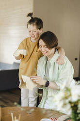Smiling mother and son holding pizza doughs at home - SEAF00266
