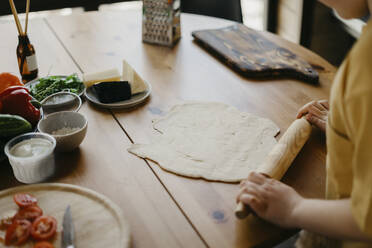 Junge bereitet Pizzateig mit Nudelholz auf einem Tisch vor - SEAF00268