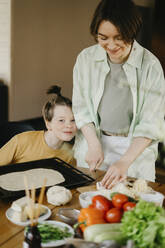 Lächelnde Mutter bereitet mit ihrem Sohn zu Hause eine Pizza zu - SEAF00270