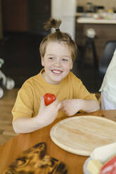 Smiling boy holding tomato at home - SEAF00272