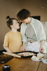 Smiling son looking at mother preparing pizza on table - SEAF00276