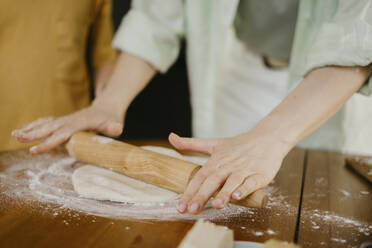 Frau drückt Pizzateig mit einem Nudelholz auf einem Tisch flach - SEAF00278